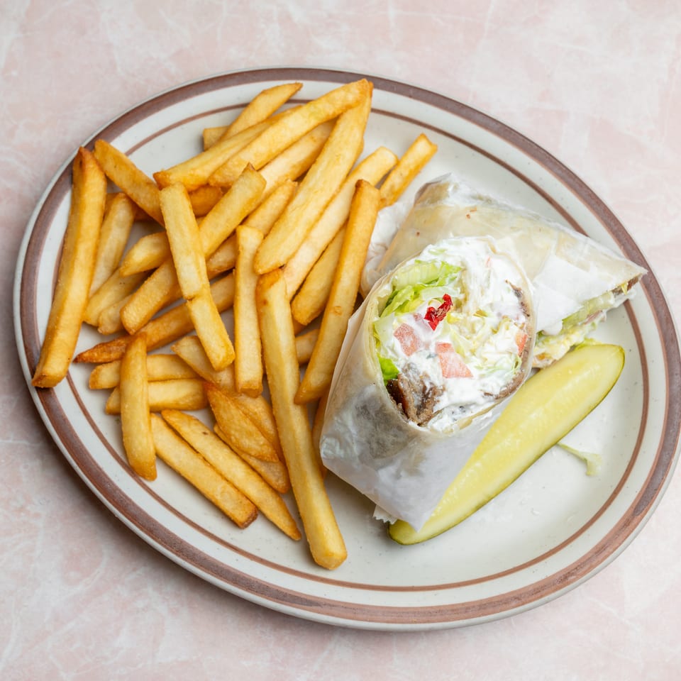 Plate of golden French fries, a loaded burger with lettuce and sauce, and a pickle spear.