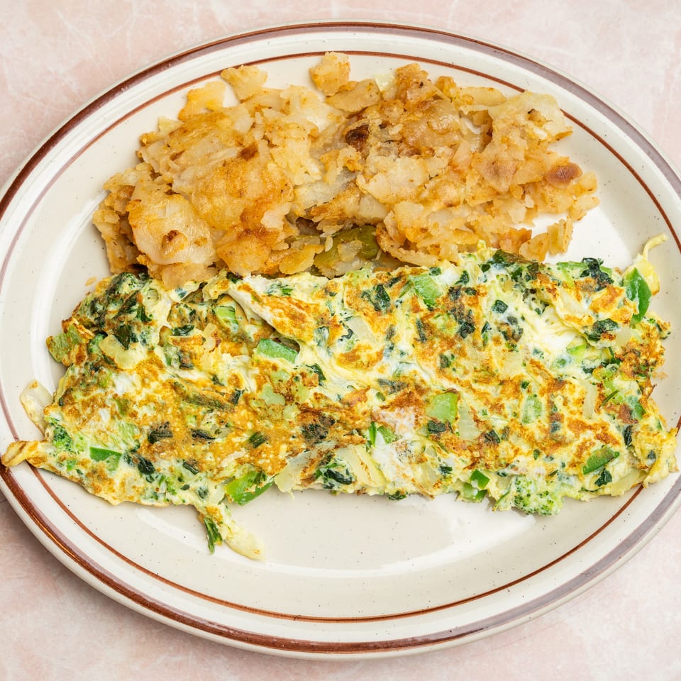 Plate of golden vegetable omelet with broccoli and green peppers, served alongside crispy fried potatoes.
