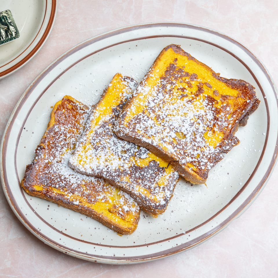 Golden French toast slices dusted with powdered sugar on a vintage oval plate.