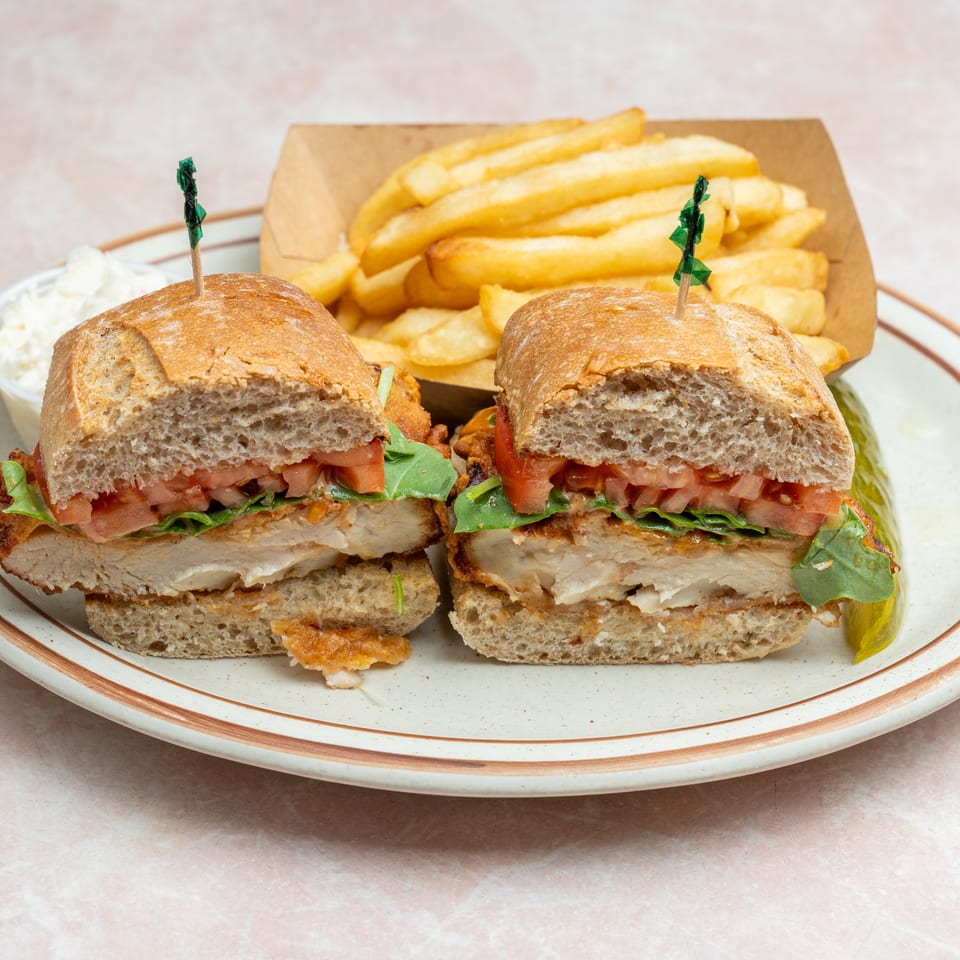 Two toasted chicken sandwiches with lettuce and tomatoes served alongside fries, coleslaw, and a pickle.