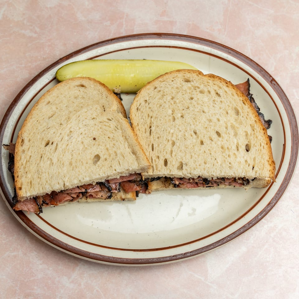 Sliced roast beef sandwiches on toasted bread served with a pickle spear on a vintage plate.