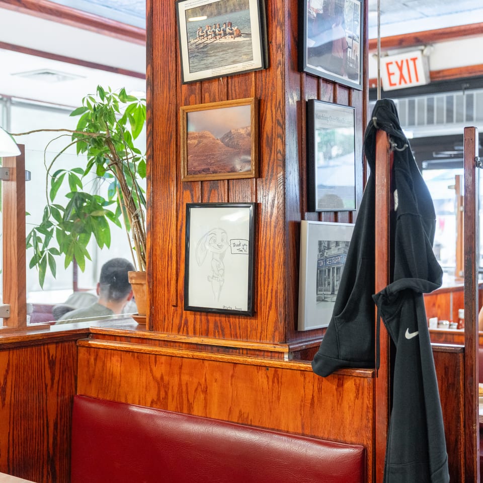Restaurant interior with wood-paneled walls, framed artwork, red booths, hanging lamps, potted plant, and diners.