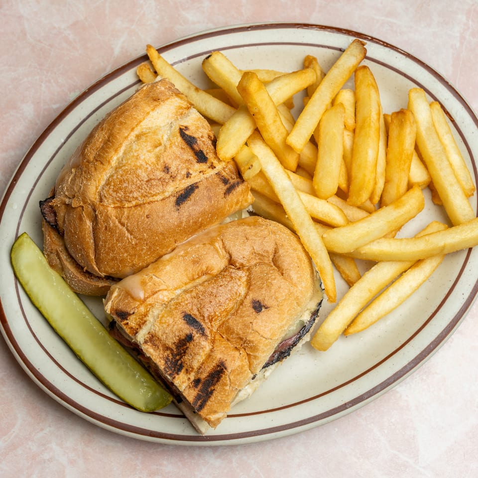 Two grilled sandwiches with golden fries and a pickle spear on a retro oval plate.