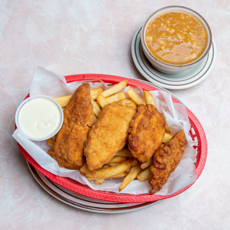 Red basket of fried fish and chicken with French fries, dipping sauce, and a bowl of creamy soup.