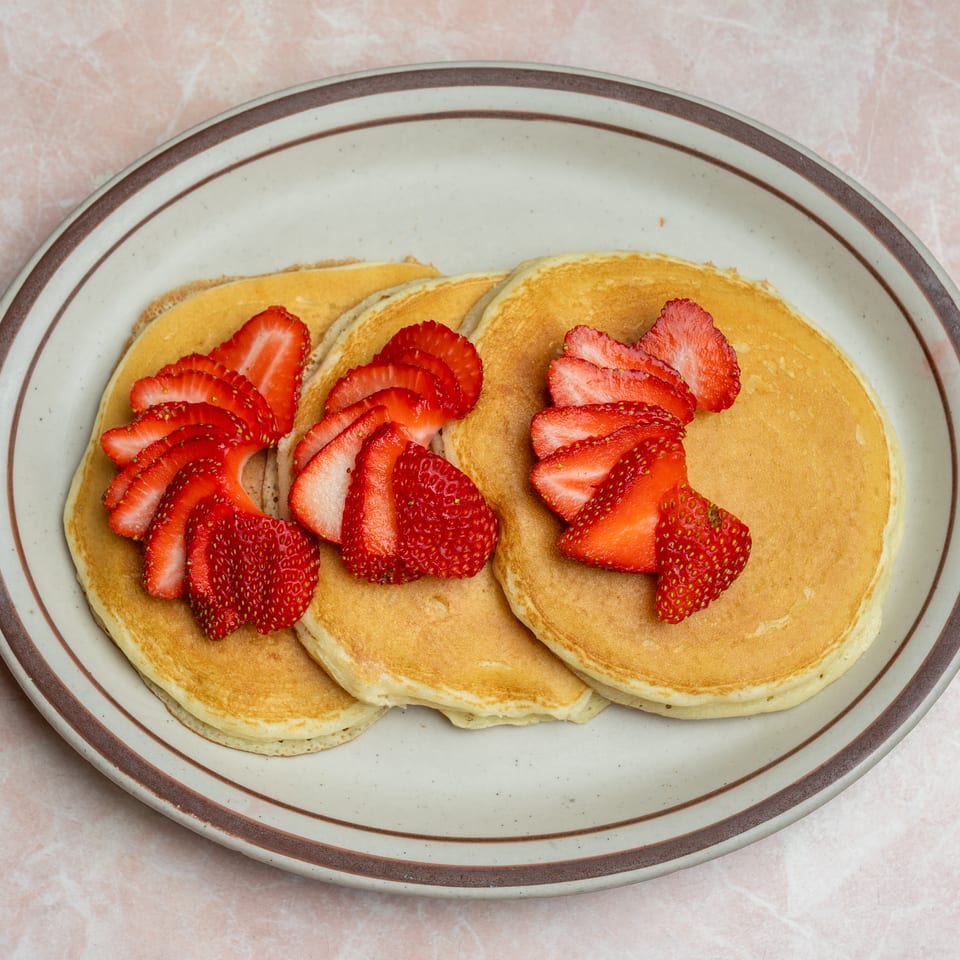 Stack of golden pancakes topped with sliced fresh strawberries on a large ceramic plate.