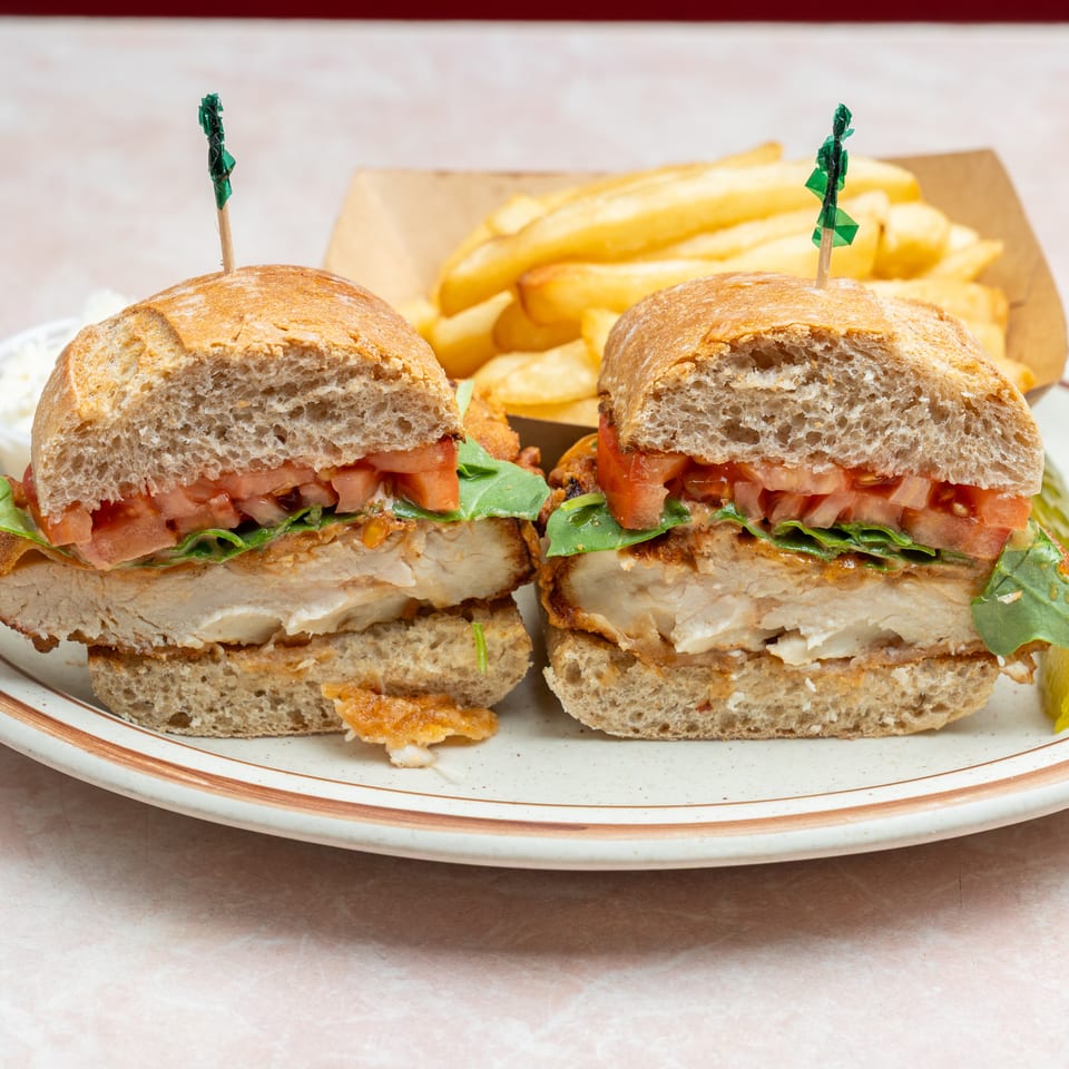 Two toasted chicken sandwiches with lettuce and tomato, served with thick-cut fries and a side of coleslaw.